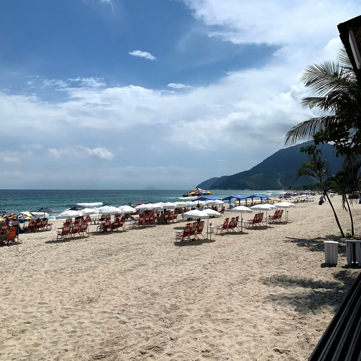 Faixa de areia com guarda-sóis e morro ao fundo