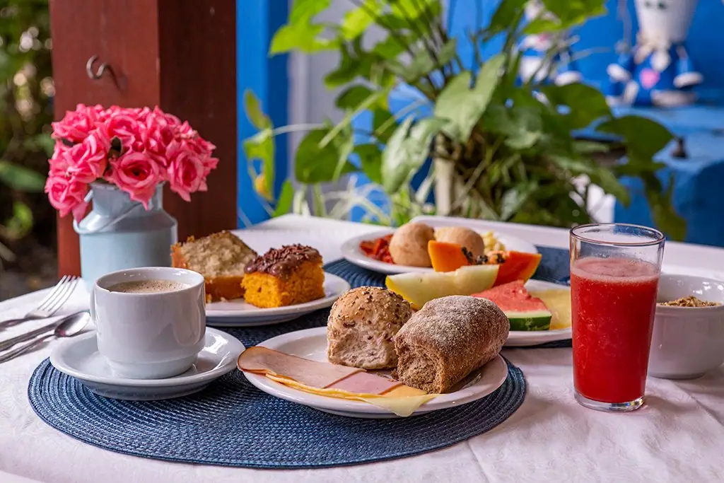 Mesa de café da manhã com pães, bolo, frutas e suco